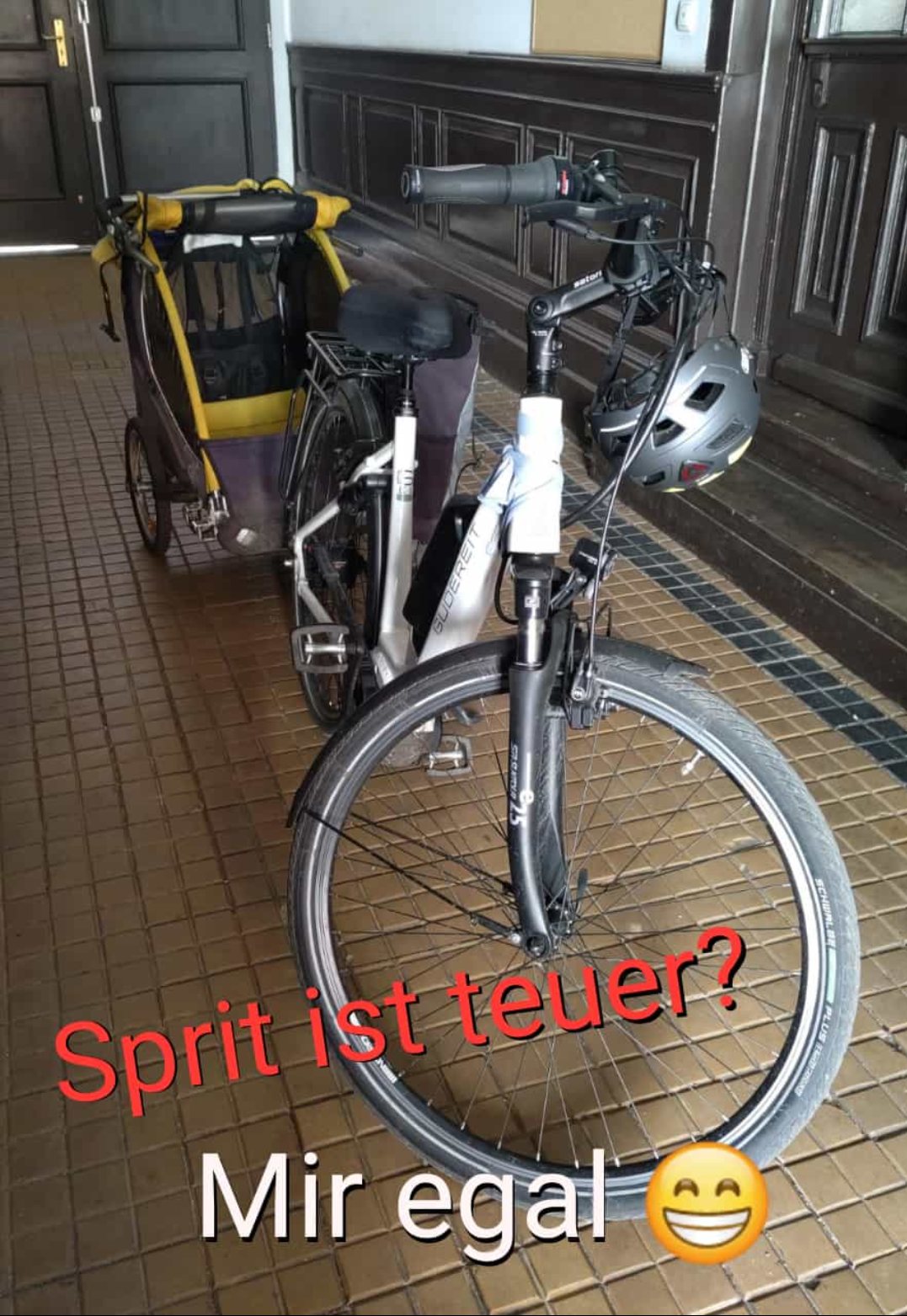 Ein Fahrrad mit Fahrradanhänger. Darüber steht der Text: "Sprit ist teuer? Mir egal. 😁"